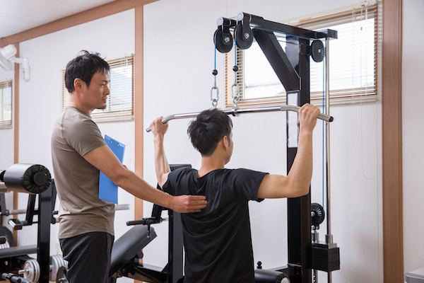 パーソナルトレーナーが男性のラットプルダウンを補助している写真です。
