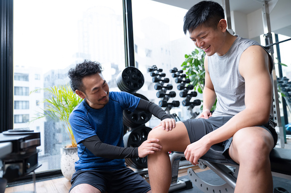 パーソナルジムでトレーナーが男性の膝の状態をチェックしながら話している写真です。