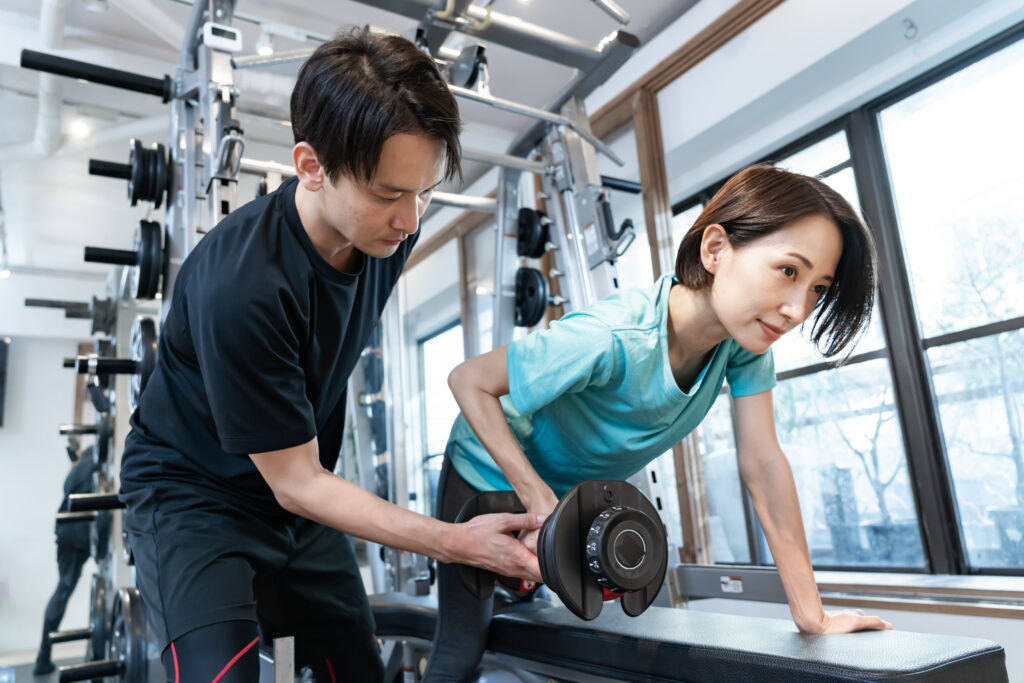 アスレティックトレーナーの男性が女性のトレーニングの補助をしている写真です。