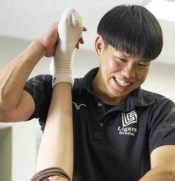 スポーツトレーナーの男性がストレッチの補助をしている写真です。